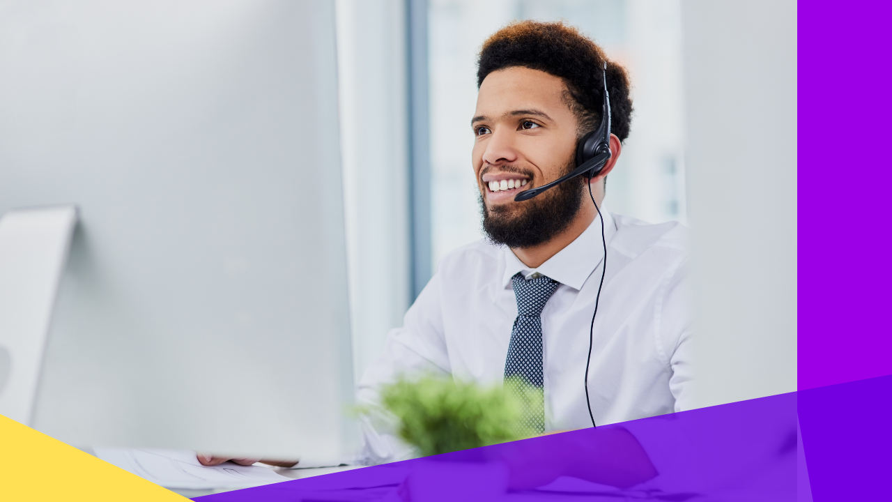 A man wearing a headset smiles while working at his computer.