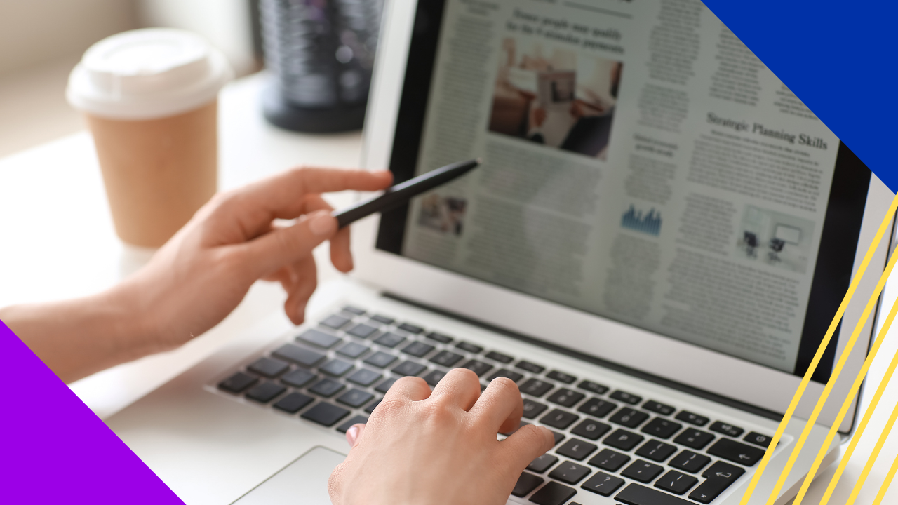 A person is using a laptop with one hand on the keyboard and the other holding a pen to point at the screen, with a cup of coffee beside the computer.